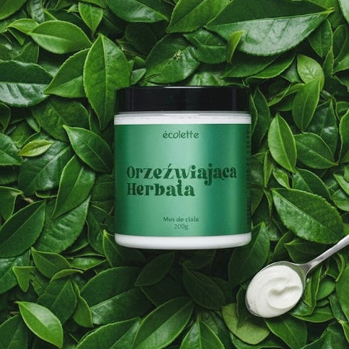 Wegański mus do ciała Orzeźwiająca Herbata Écolette w aranżacji z liśćmi herbaty podkreślającymi świeży zapach.