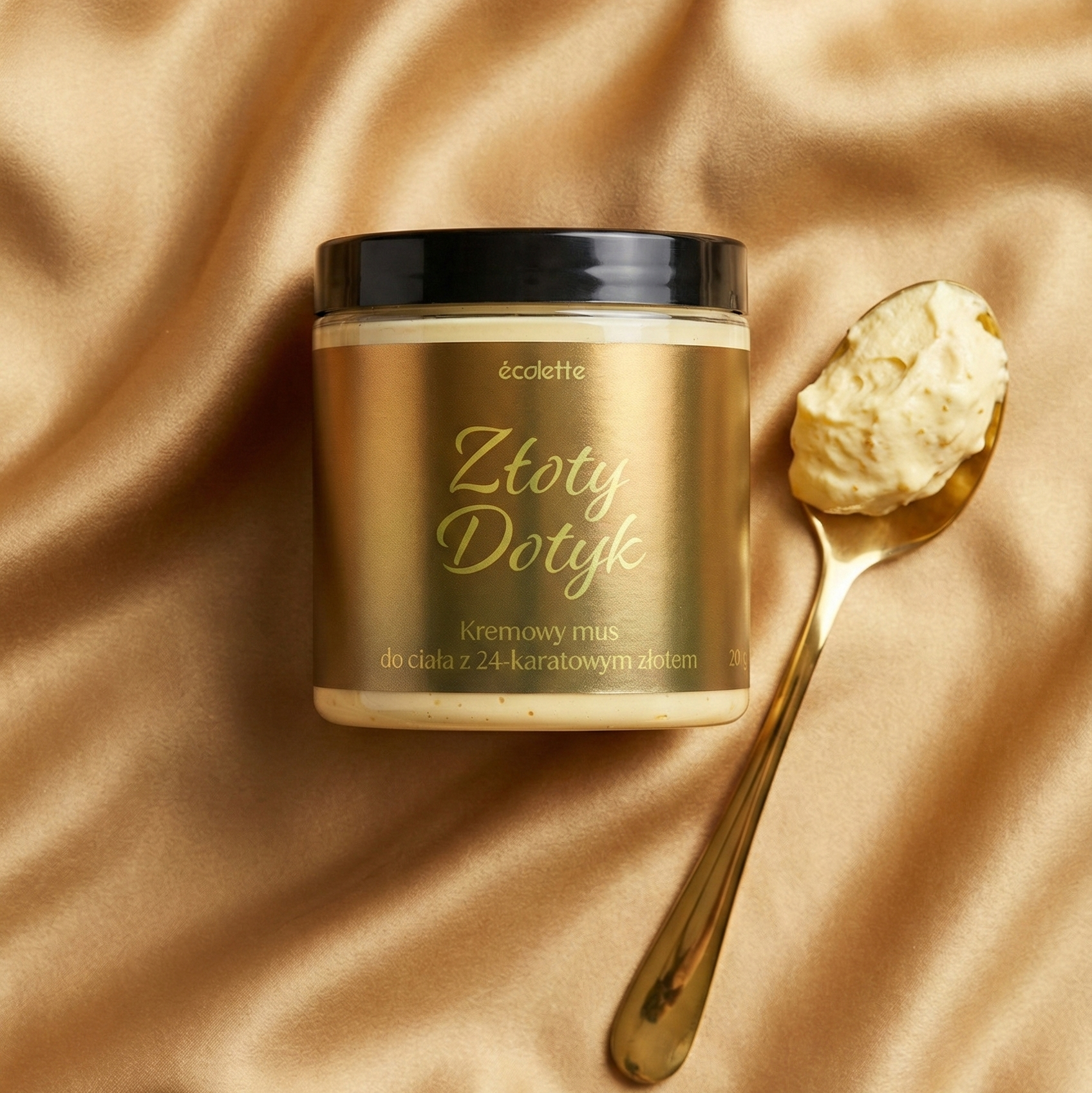 Wegański mus do ciała Złoty Dotyk Écolette na beżowej satynie, ze złotą łyżeczką podkreślającą jego elegancję.